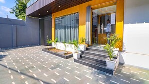 A modern building with a yellow facade, large glass windows, and a tiled patio area with potted plants. - FabHotel The Shashi - Nr. Sarnath Temple (Varanasi)