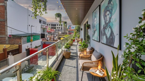 A balcony with wicker furniture, potted plants, and artwork. - FabHotel The Shashi - Nr. Sarnath Temple (Varanasi)