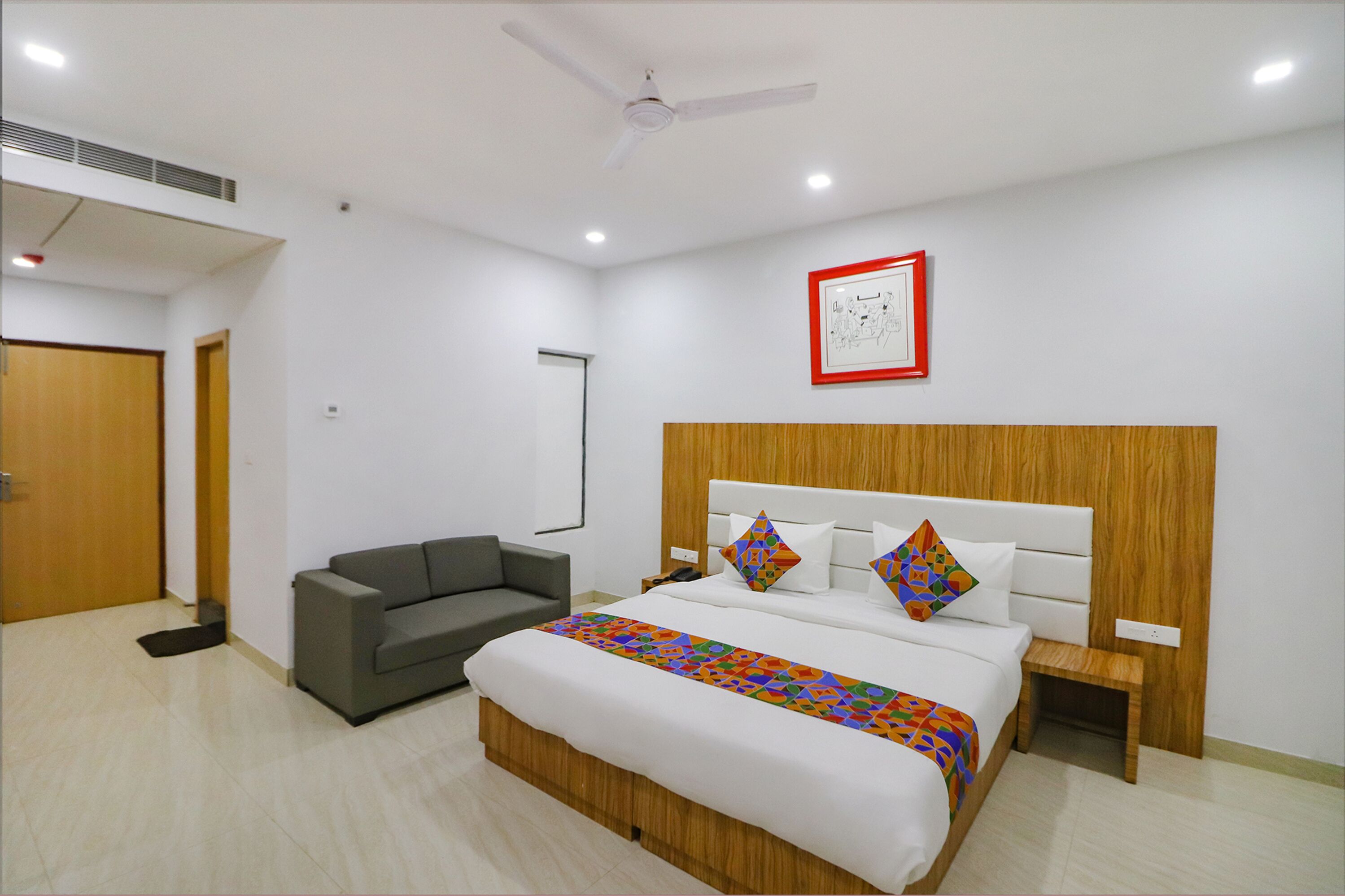 A hotel room with a bed, a sofa, a nightstand, a ceiling fan, and a framed picture on the wall.