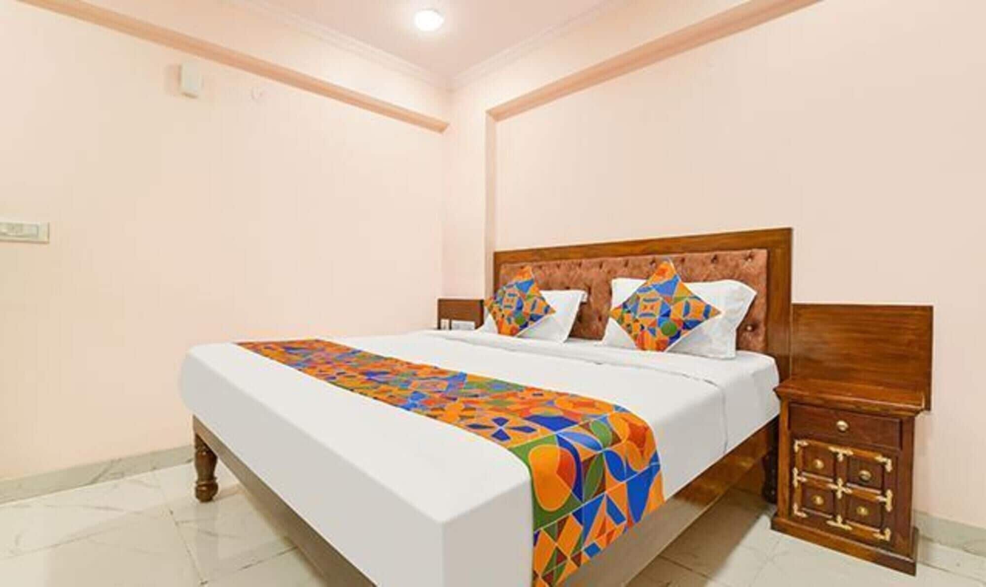 Cama bem arrumada com manta de padrão geométrico colorido, cabeceira de madeira e mesa de cabeceira com gavetas.