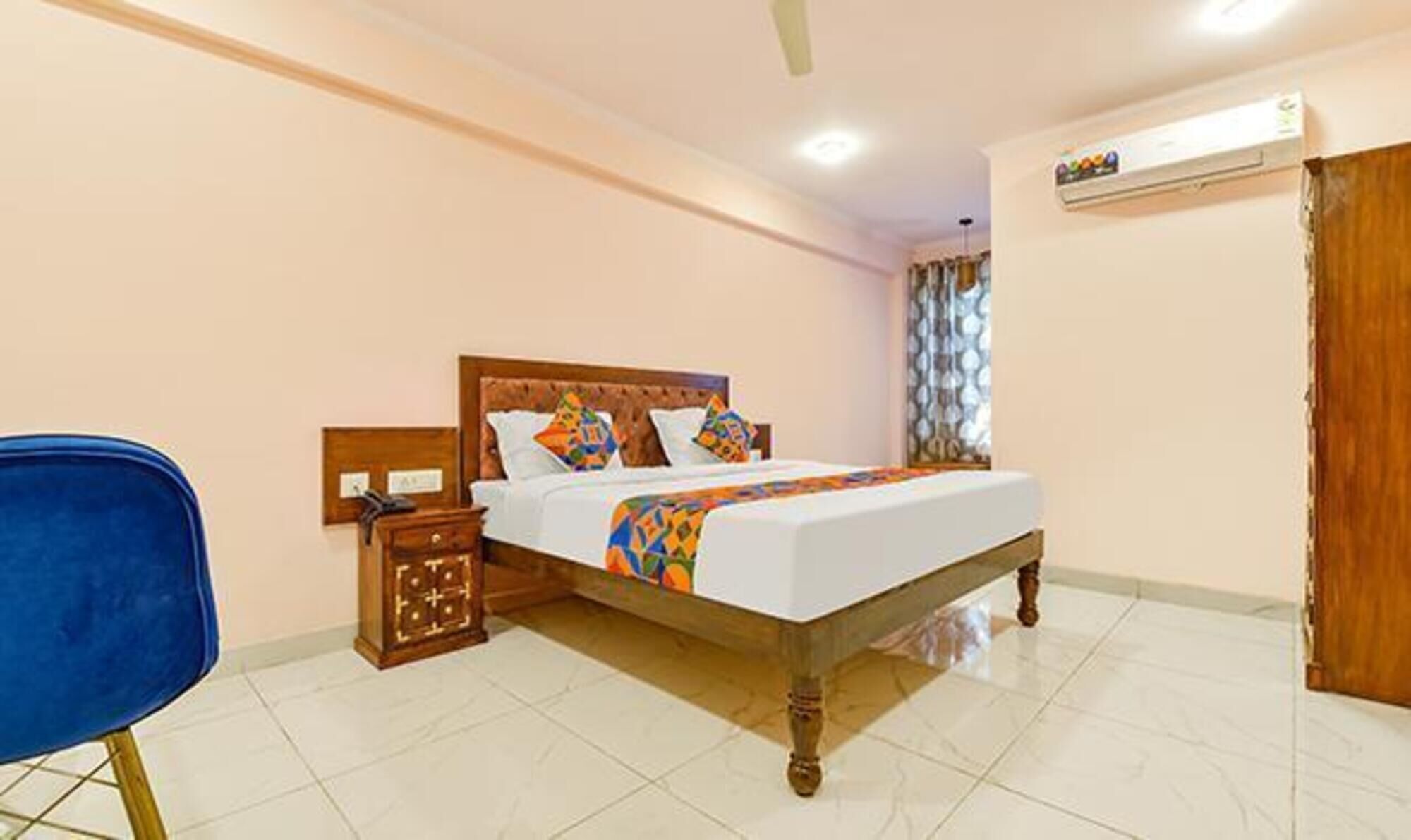 Quarto de hotel com cama de madeira, mesa de cabeceira, uma cadeira azul e piso de azulejos.
