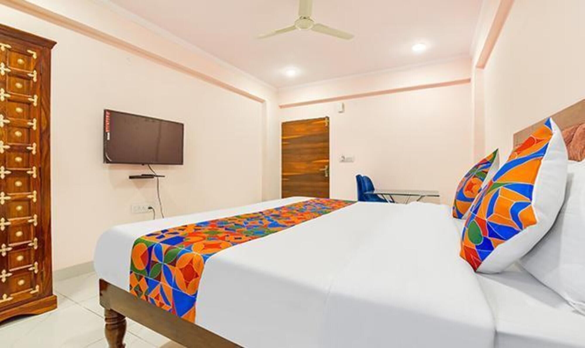 A hotel room with a bed, a television, a wooden wardrobe, and a door.