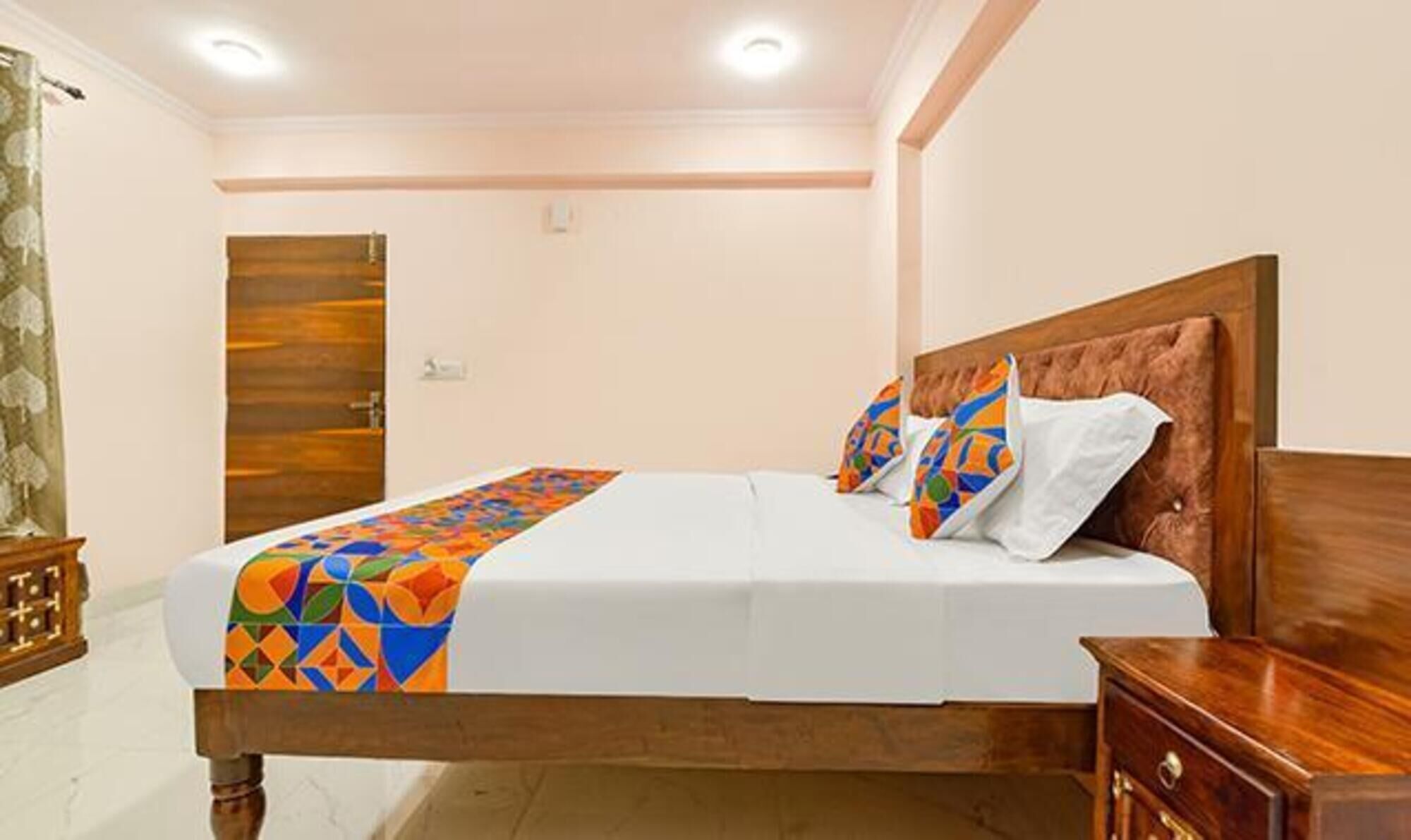 A neatly made bed with a colorful geometric bedspread, a wooden headboard, and a wooden nightstand with a drawer.