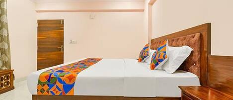 A neatly made bed with a colorful geometric bedspread, a wooden headboard, and a wooden nightstand with a drawer.