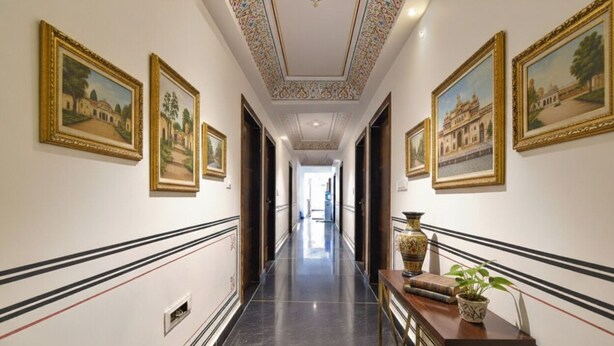 A hallway with framed artwork on the walls, a marble floor, and a wooden console table with a plant. - FabHotel JBS Heritage (Jaipur)