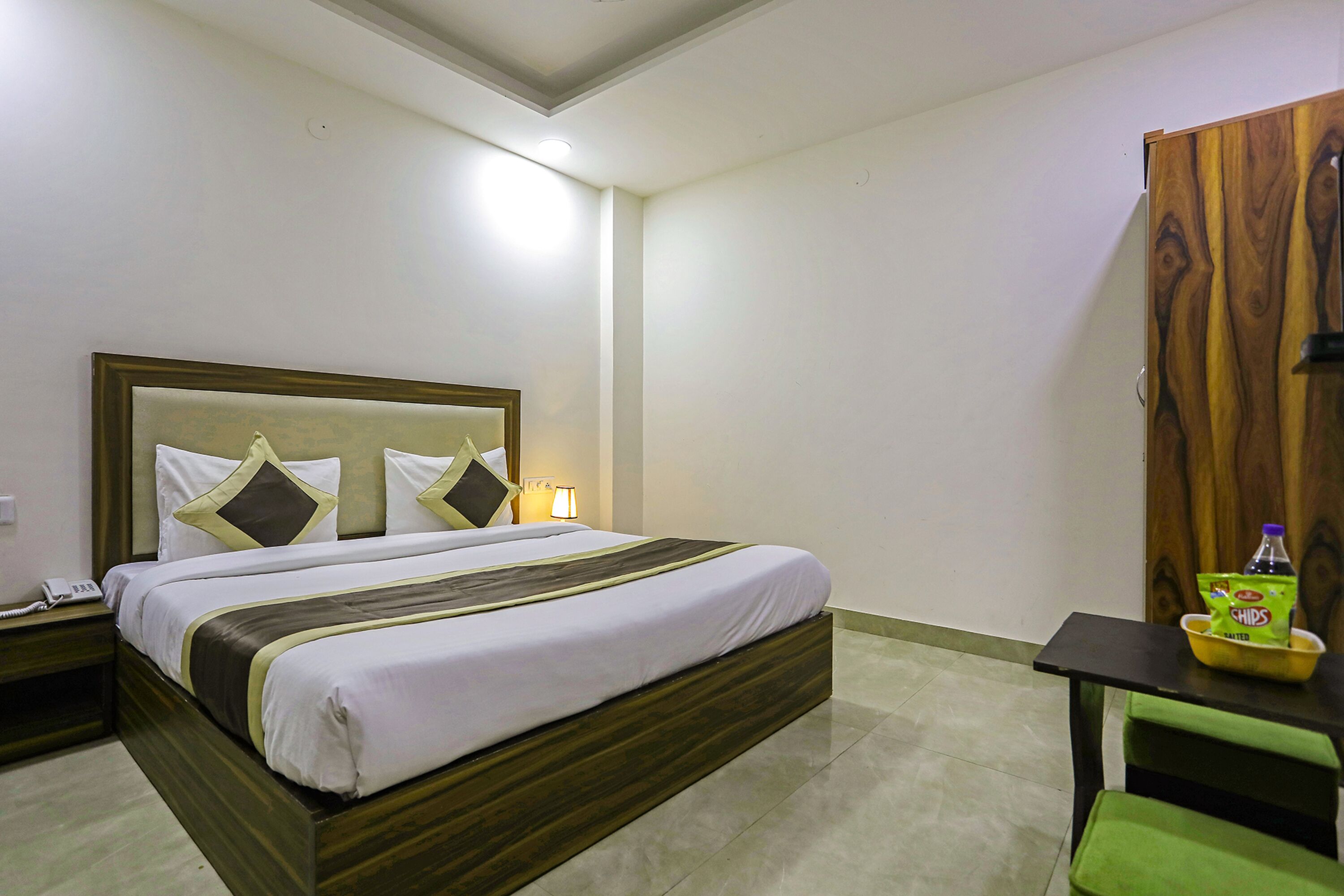 A hotel room with a large bed, bedside table, and a small table with snacks.