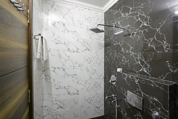 A bathroom with marble walls, a shower, and a wooden door. - FabHotel White House BNB - Nr. Yashobhoomi Convention Centre (New Delhi)