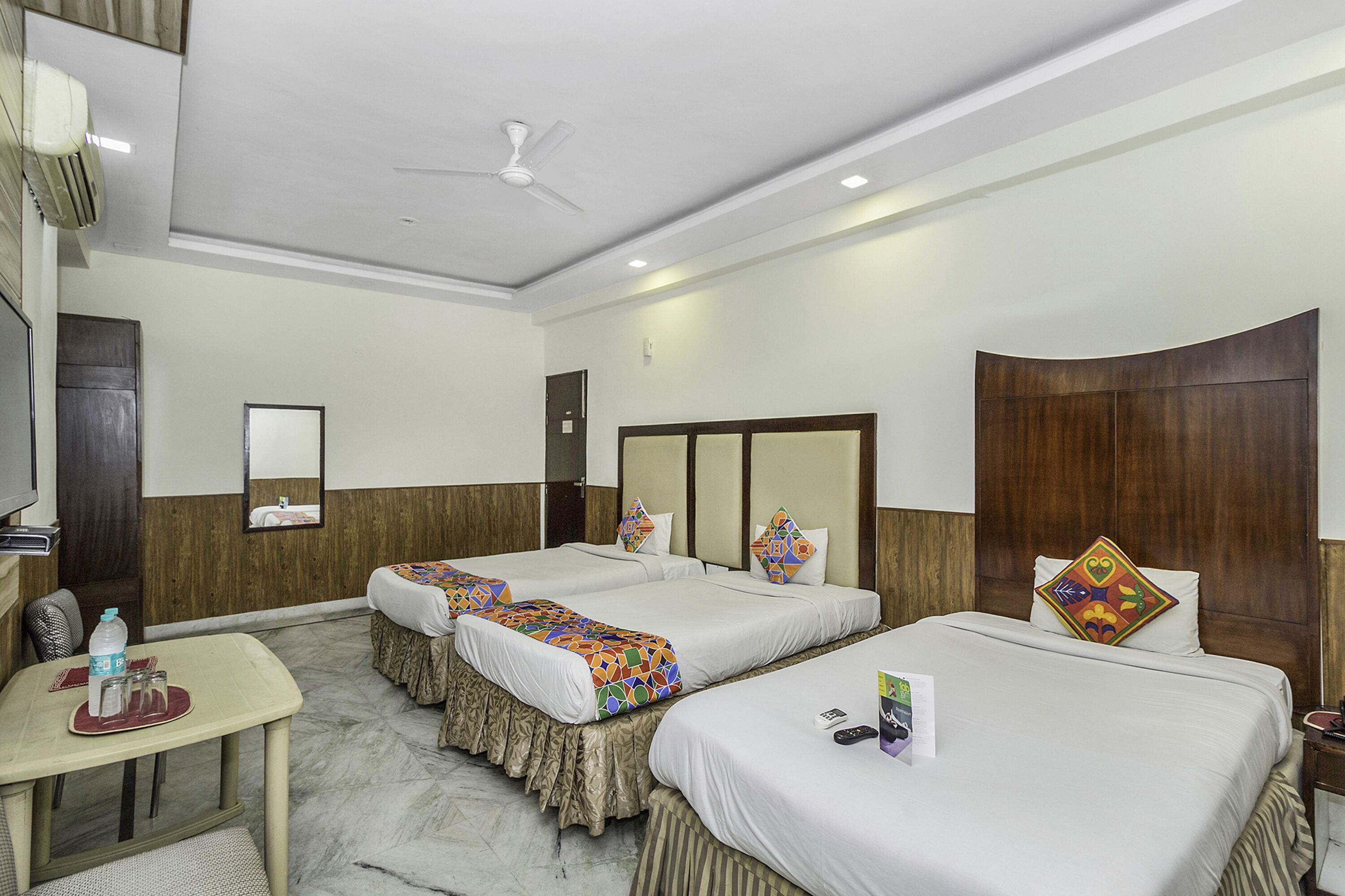 A hotel room with two beds, a desk, a chair, a table, and a ceiling fan.