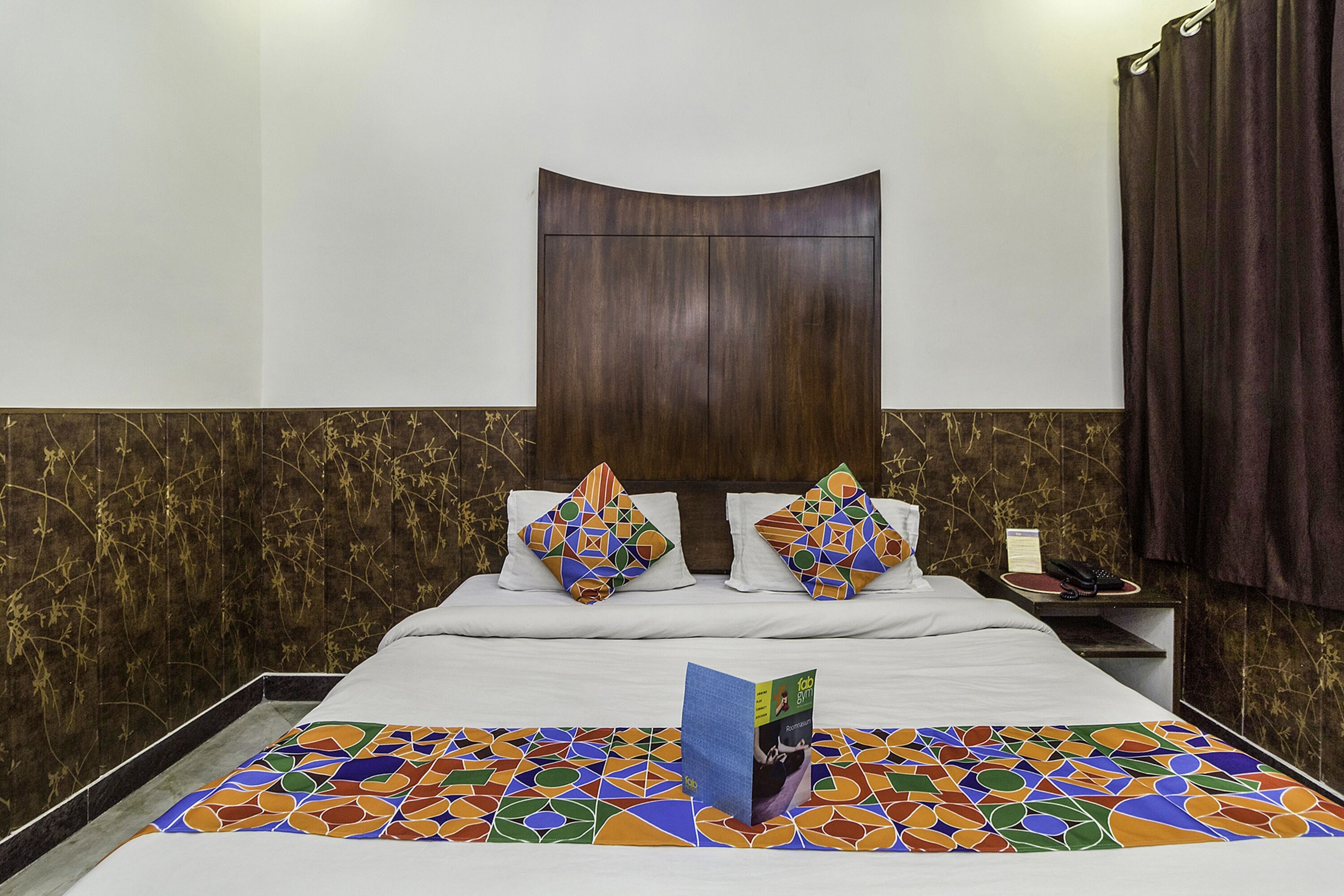 A hotel room with a bed, two decorative pillows, a nightstand, and a book on the bed.
