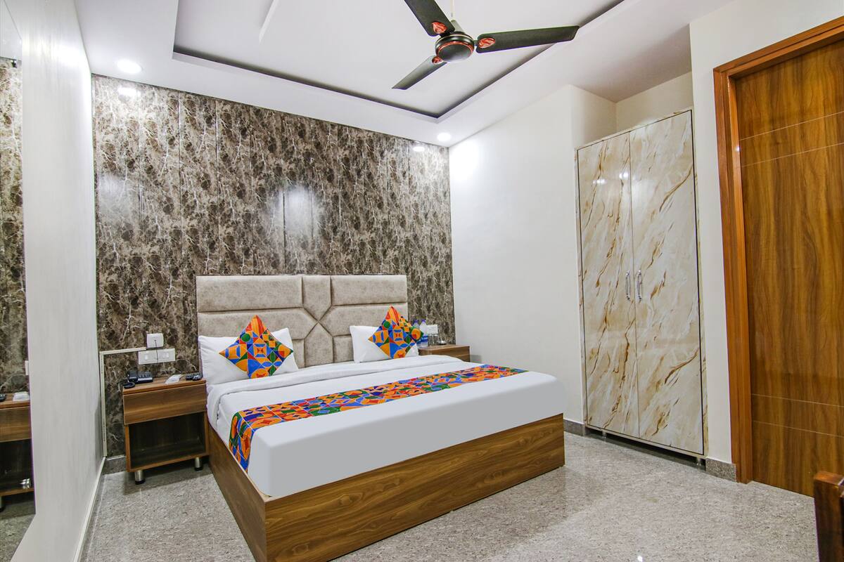 Quarto moderno com cabeceira de mármore, cama com almofadas geométricas coloridas, mesa de cabeceira de madeira e guarda-roupa com acabamento em mármore.