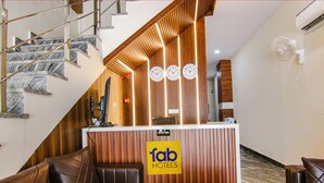 Ein Hotel-Empfangsbereich mit einem Holzbüro, einer Empfangstafel, einer Uhr und einer Treppe.