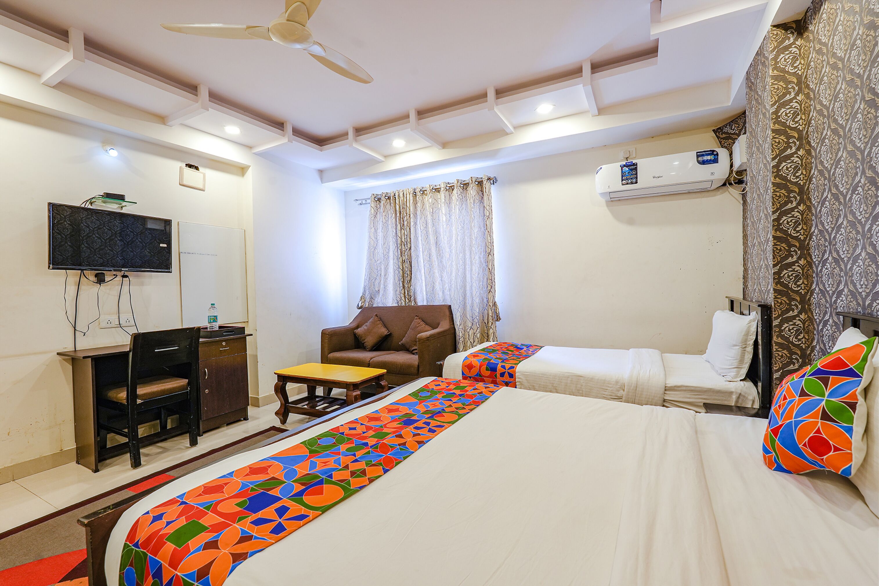 Een hotelkamer met twee bedden, een bureau, een stoel, een televisie en een airconditioner.