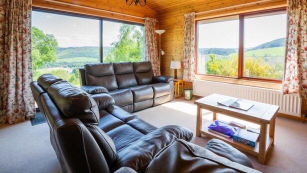 Ein gemütliches Wohnzimmer mit Ledersofa, Holztisch und großen Fenstern mit herrlichem Blick auf die Landschaft.