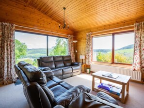 Ett mysigt vardagsrum med en soffa i läder, ett soffbord i trä och stora fönster som erbjuder en vacker utsikt över landskapet.