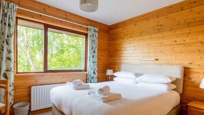 Ein Schlafzimmer mit Holzvertäfelung, einem großen Bett, einem Fenster mit Vorhängen, einem Nachttisch und einem Heizkörper.