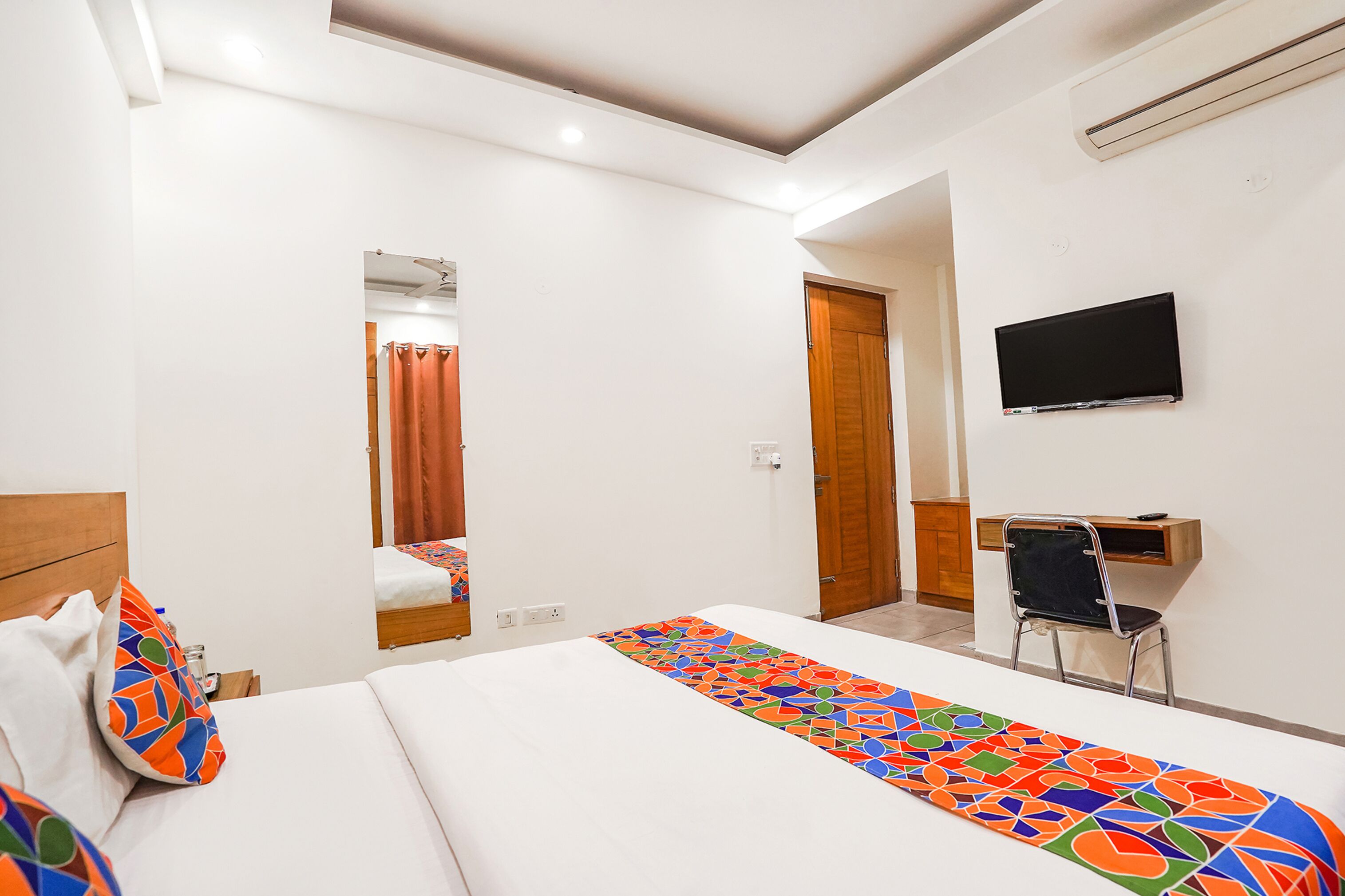 Habitación de hotel con cama, escritorio con silla, televisor y baño visible a través de una puerta abierta.