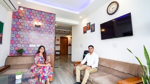 A modern hotel lobby with a patterned wall, a sofa, a coffee table, and a television. - Fabhotel Emoji Stays (Gurugram)