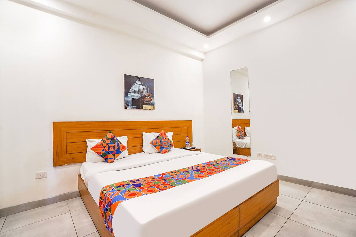 Una habitación de hotel moderna con una cama grande, cabecero de madera, paredes blancas y un cuadro enmarcado en la pared.