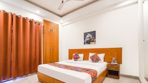 A bedroom with a large bed, wooden headboard, and a nightstand with a bottle and glasses. - Fabhotel Emoji Stays (Gurugram)