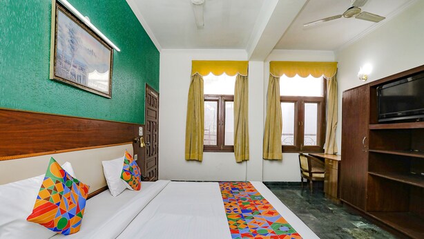A hotel room with a bed, a desk, a TV, and a window with curtains. - Fabexpress Primero I (Gurugram)