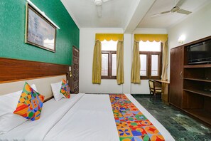 Habitación de hotel con cama, escritorio, televisión y ventana con cortinas.