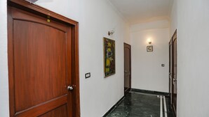 A hallway with wooden doors, a marble floor, and wall-mounted light fixtures. - Fabexpress Primero I (Gurugram)