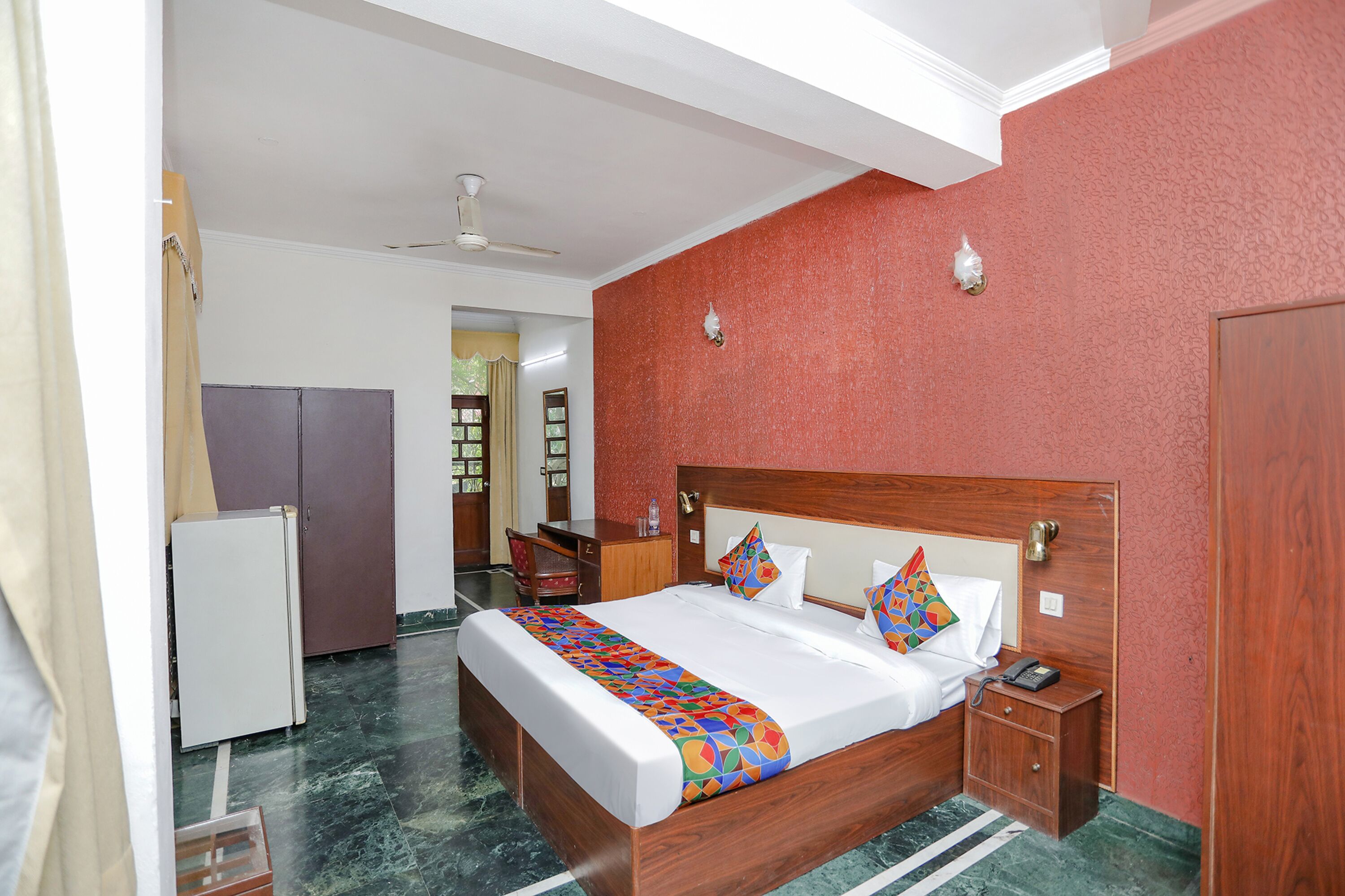 A hotel room with a large bed, a wooden nightstand, a desk, and a wardrobe.