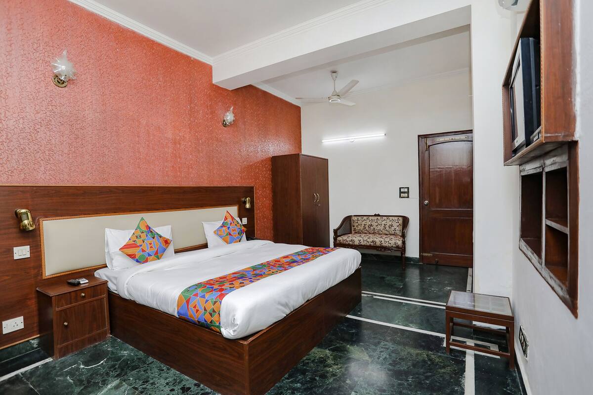 A hotel room with a wooden bed, a nightstand, a wardrobe, a chair, and a television on the wall.