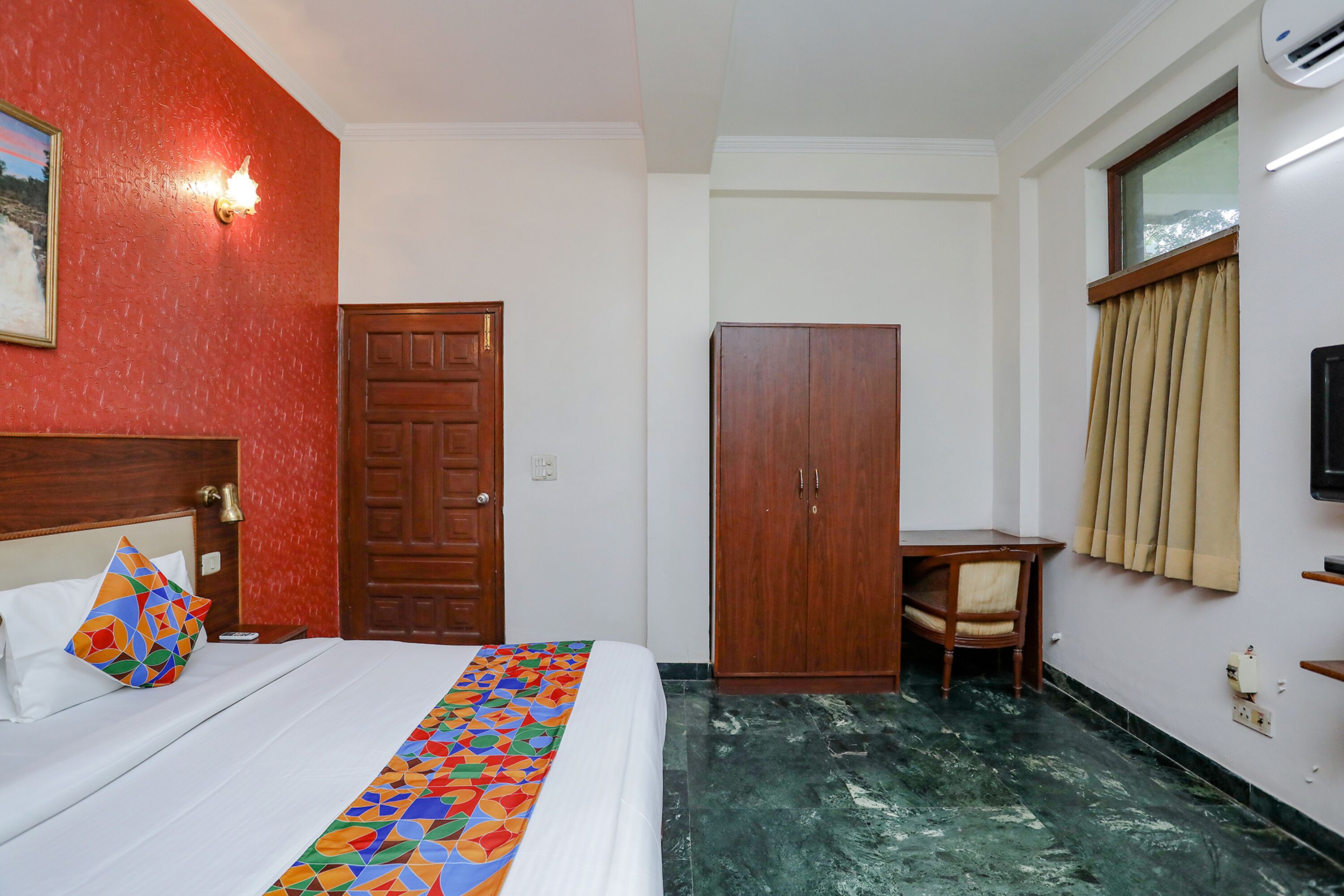 Een hotelkamer met een bed, een houten kledingkast, een klein tafeltje met een stoel en een raam met gordijnen.