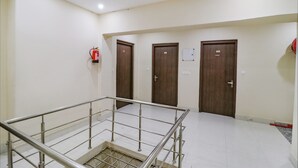 A hotel corridor with three wooden doors, a fire extinguisher, and a metal railing. - Fabexpress Kartikey Inn (Haridwar)