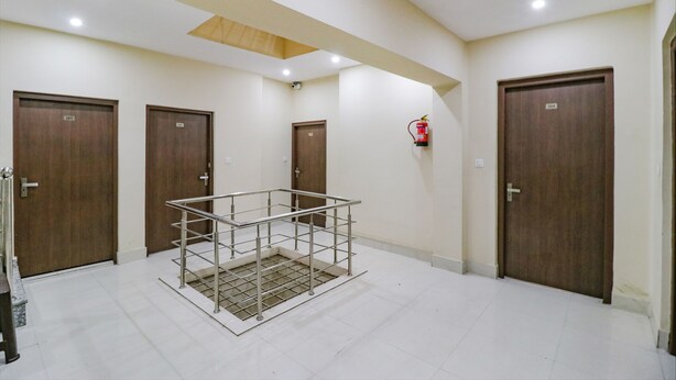 A hotel corridor with four wooden doors, a metal railing, and a fire extinguisher on the wall. - Fabexpress Kartikey Inn (Haridwar)