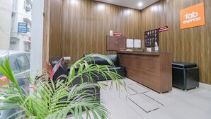A reception area with a wooden wall, a reception desk, a black leather sofa, a potted plant, and a sign for 'fab express'. - Fabexpress Kartikey Inn (Haridwar)