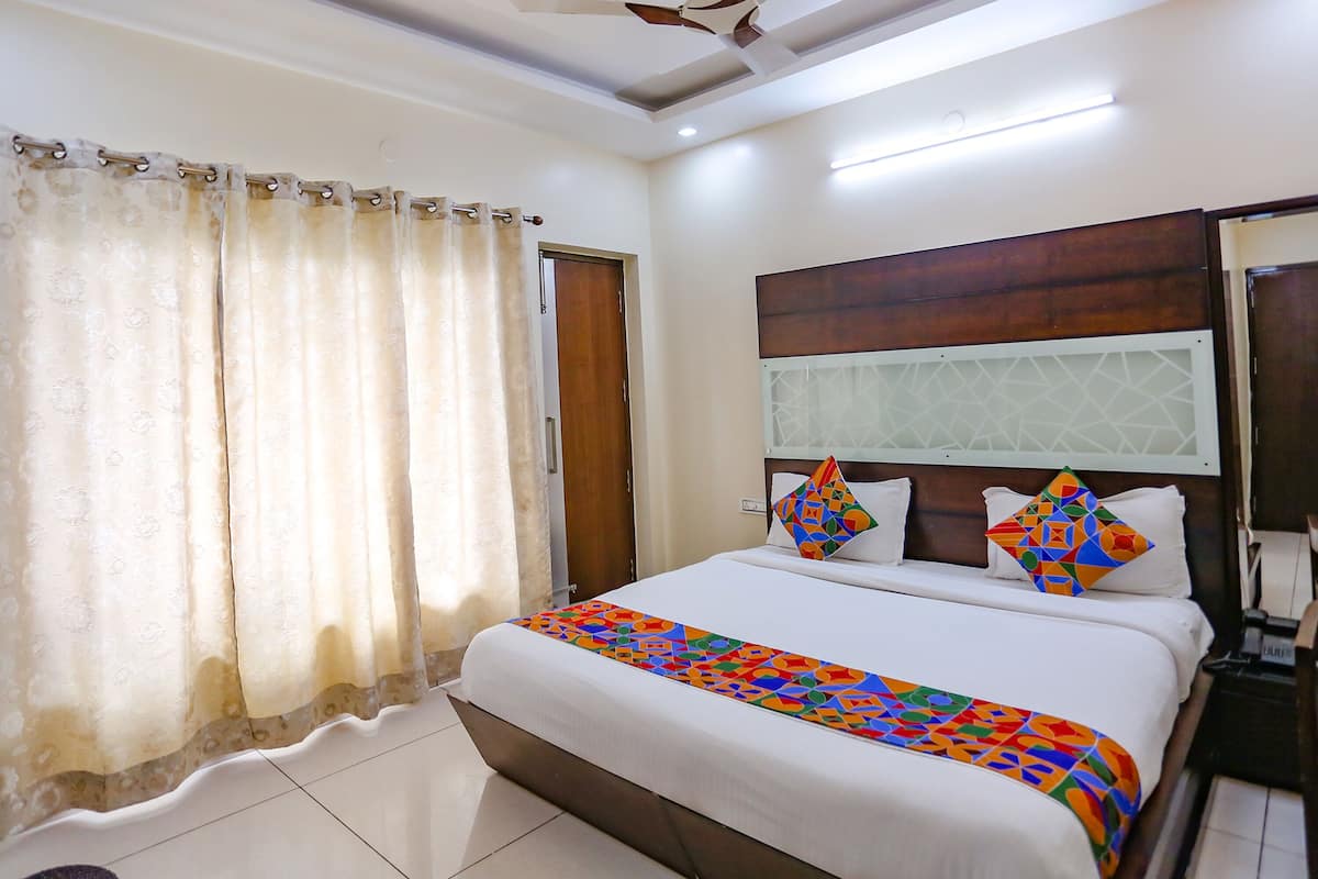 Quarto de hotel com cama, cortinas, cabeceira de madeira e mesa de cabeceira.