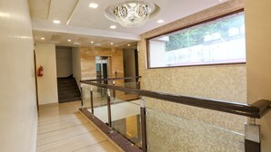 A modern interior with a glass railing, a chandelier, and a view through a window. - FabHotel Winterline Inn (Dehradun)