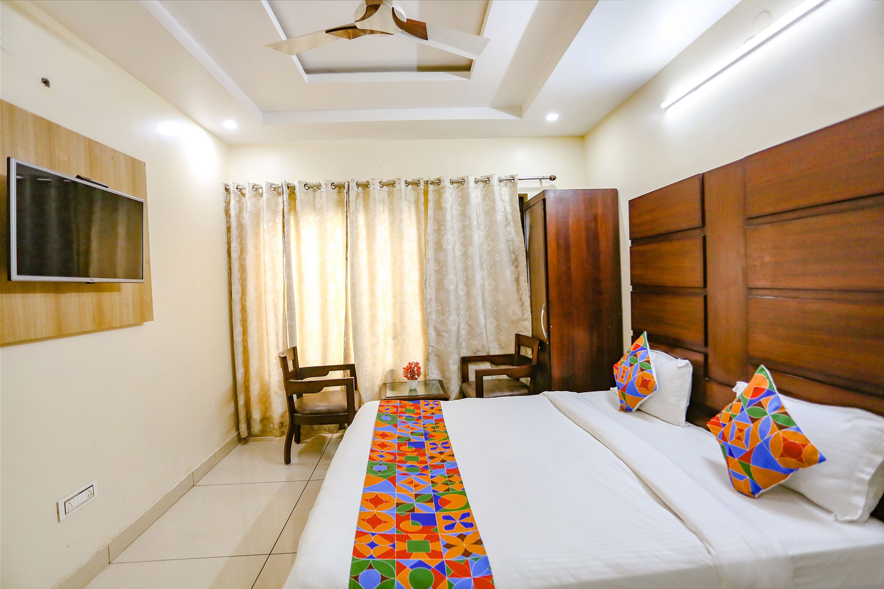 A hotel room with a bed, two chairs, a TV, and a wooden headboard.