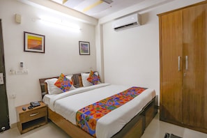 Een hotelkamer met een bed, een houten garderobe, een nachtkastje en een airconditioner aan de muur.