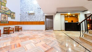 A hotel lobby with a herringbone-patterned floor, wooden chairs, a reception desk, and a staircase. - FabHotel Classic Holiday (Jaipur)