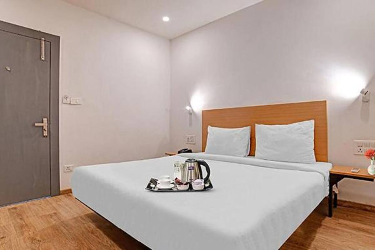 Quarto de hotel com cama grande, mesa de cabeceira com abajur e cafeteira na mesa.