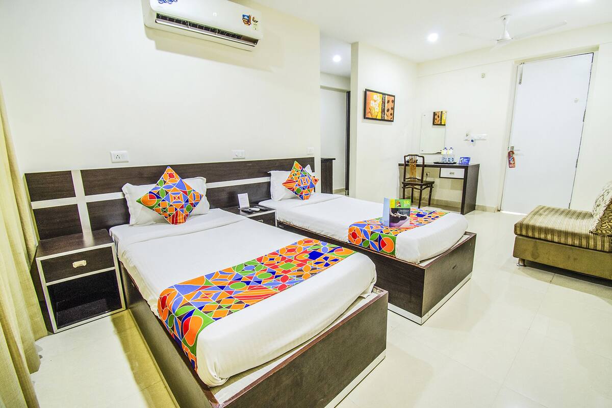Quarto de hotel com duas camas, uma escrivaninha, uma cadeira e um guarda-roupa.