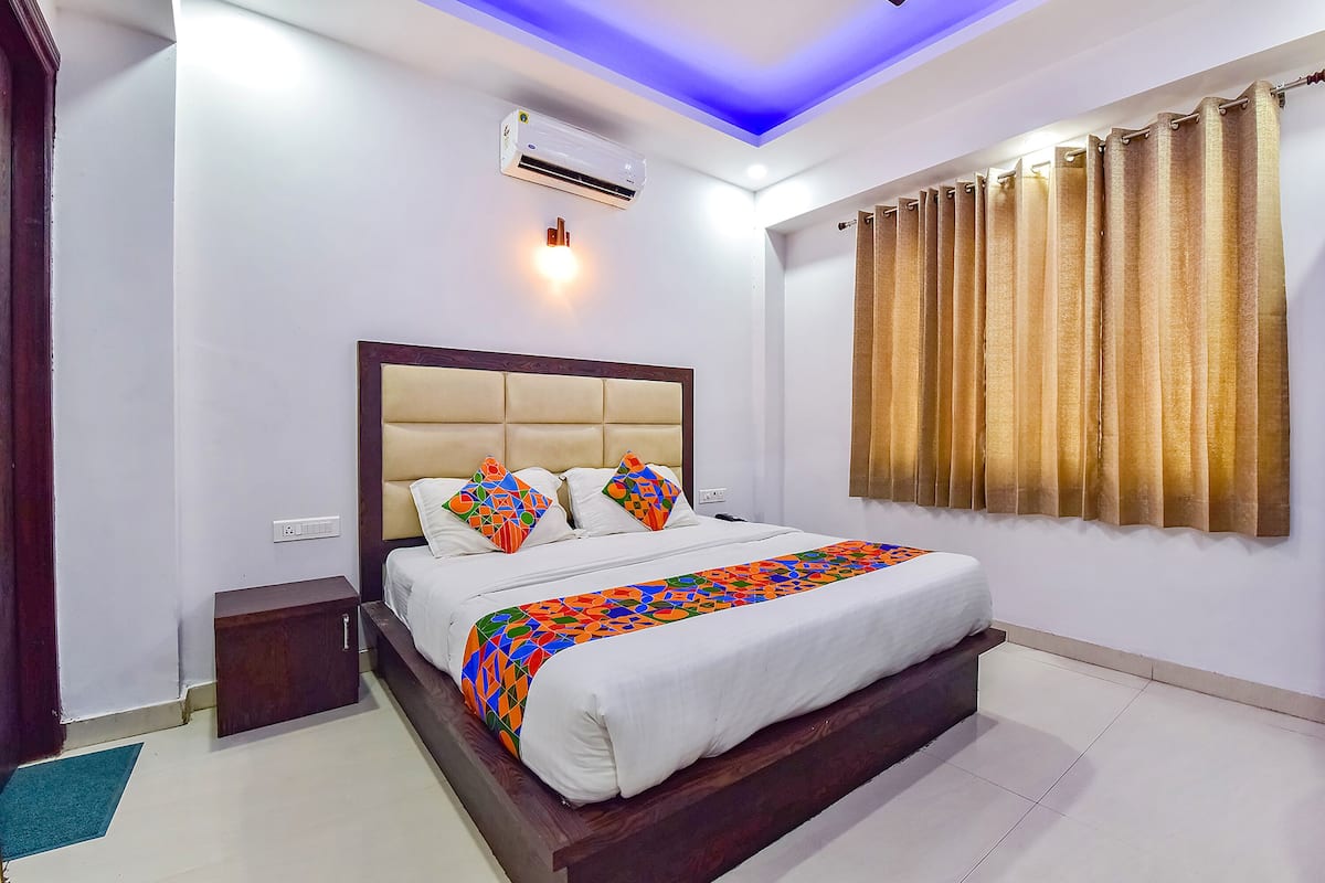 A neatly made bed with a colorful blanket, a wooden nightstand, a wall-mounted air conditioner, and a ceiling light.