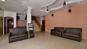 A spacious lobby with two leather sofas, a staircase, and a tiled floor. - Fabexpress Central Park (Dehradun)