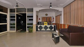 A hotel lobby with a reception desk, a brown leather sofa, and a glass coffee table. - Fabexpress Central Park (Dehradun)
