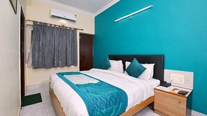 A bedroom with a bed, a nightstand, a wall-mounted air conditioner, and a curtain. - Fabexpress Central Park (Dehradun)
