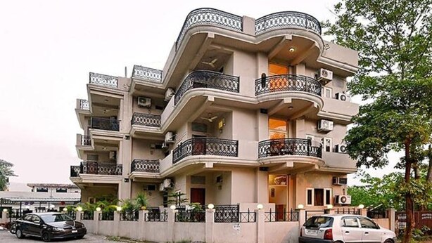 A multi-story residential building with balconies, a gated entrance, and parked cars. - Fabexpress Central Park (Dehradun)