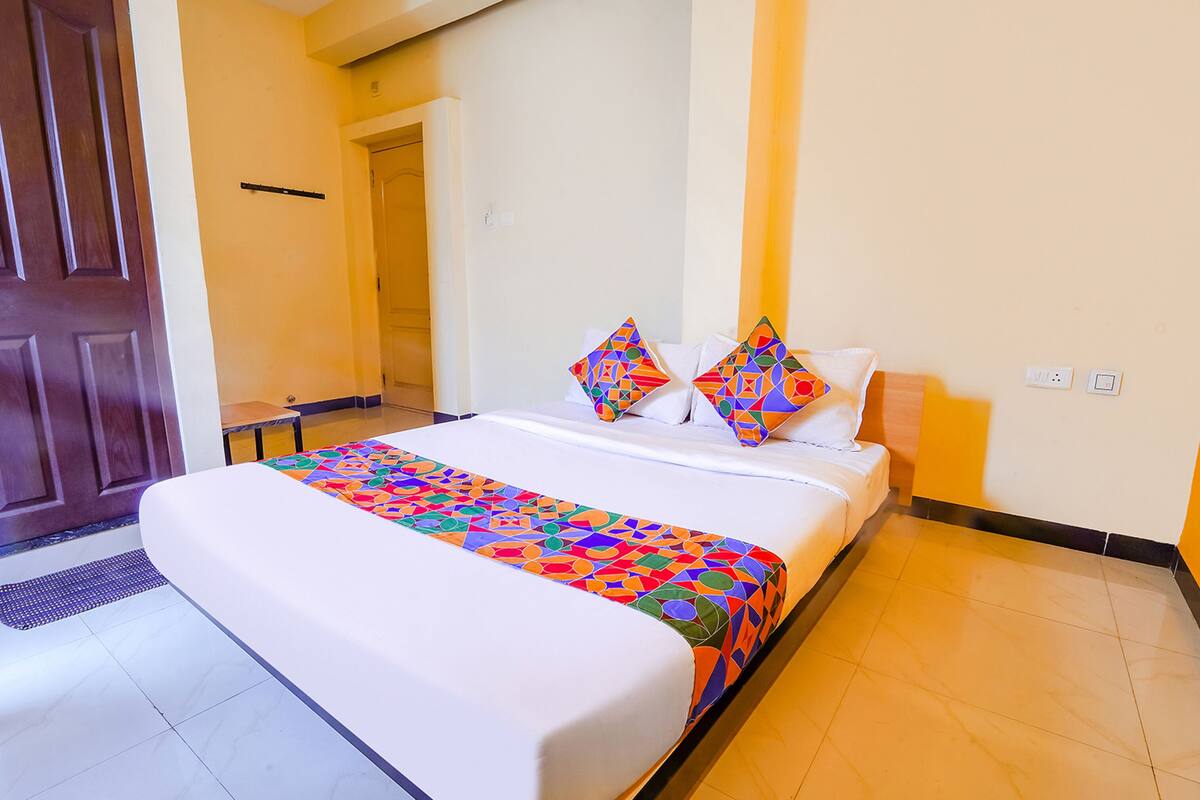 A hotel room with a large bed, colorful bedspread, and two decorative pillows.