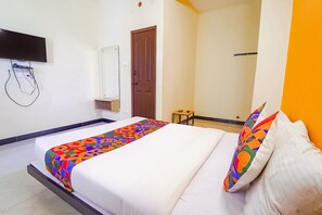 A hotel room with a bed, a TV mounted on the wall, a door, and a small table. - FabHotel Virksham (Coimbatore)
