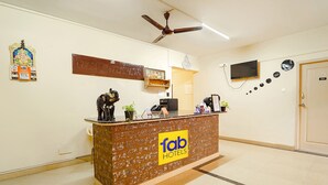 Una mesa de recepción con el logotipo de 'fab hotels', un ventilador de techo, un televisor y una puerta con el símbolo del número.