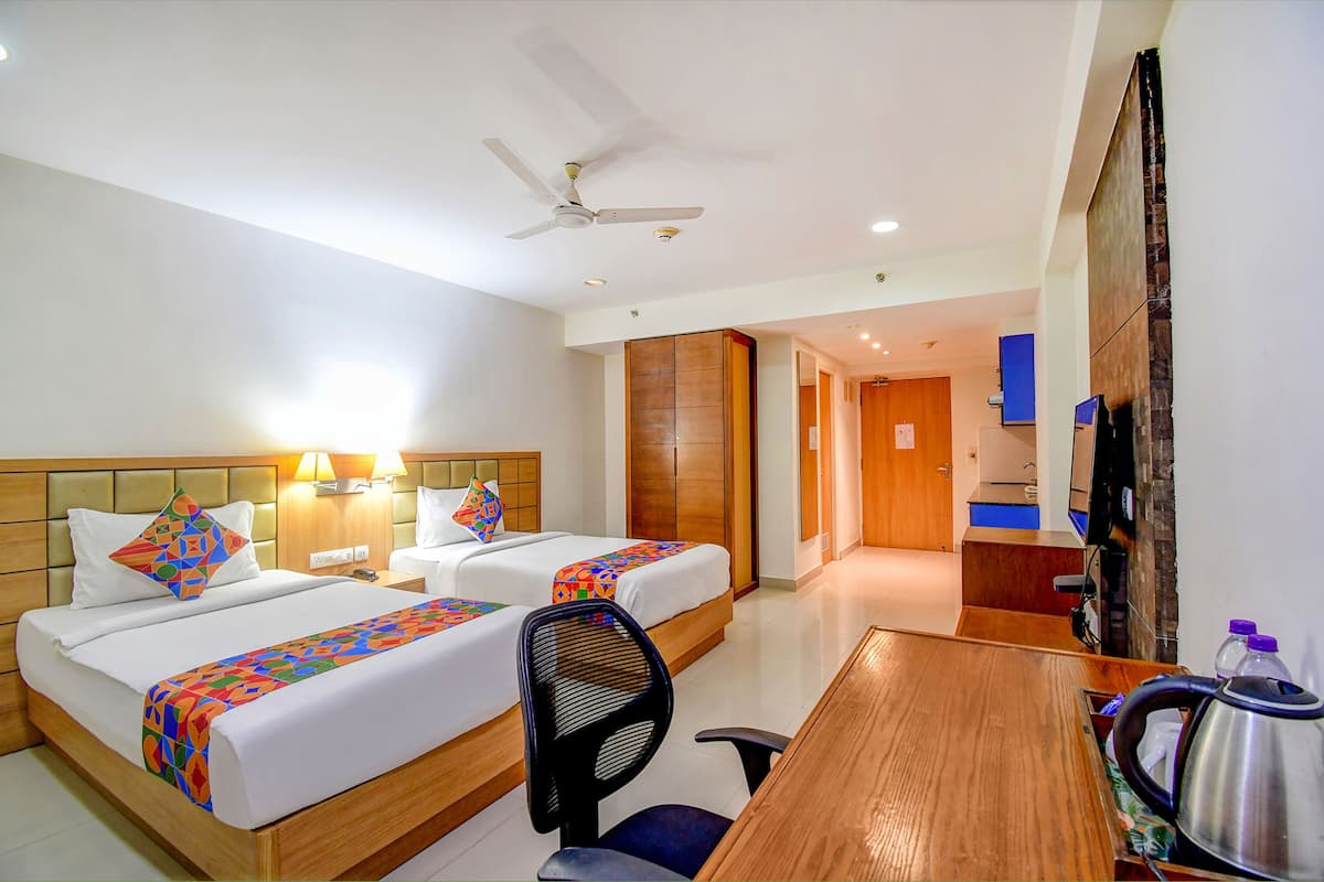 Habitación de hotel con dos camas, un escritorio, una silla, un ventilador de techo y un televisor.