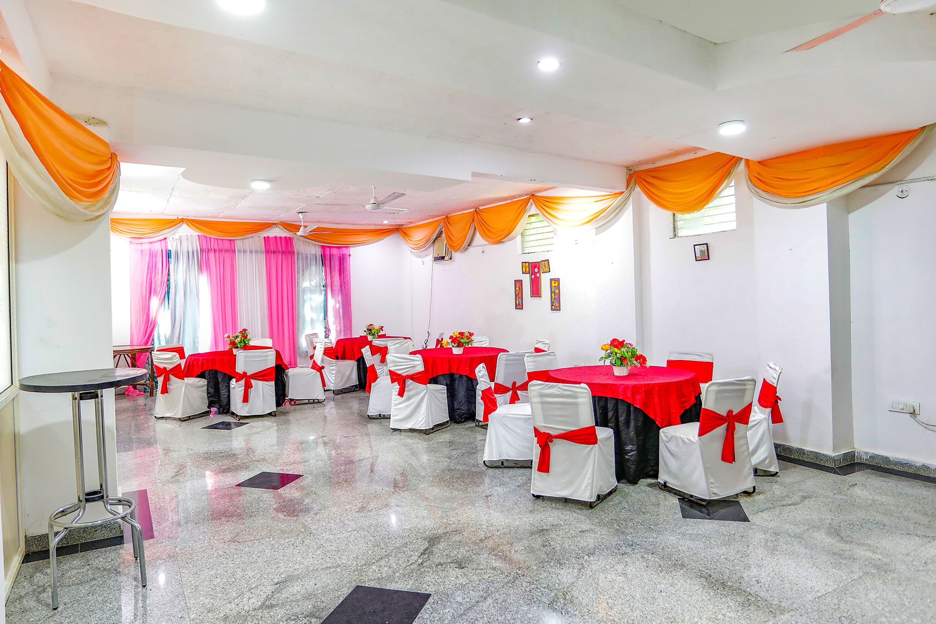 A conference room with tables and chairs, draped with orange and white fabric, and a polished floor.
