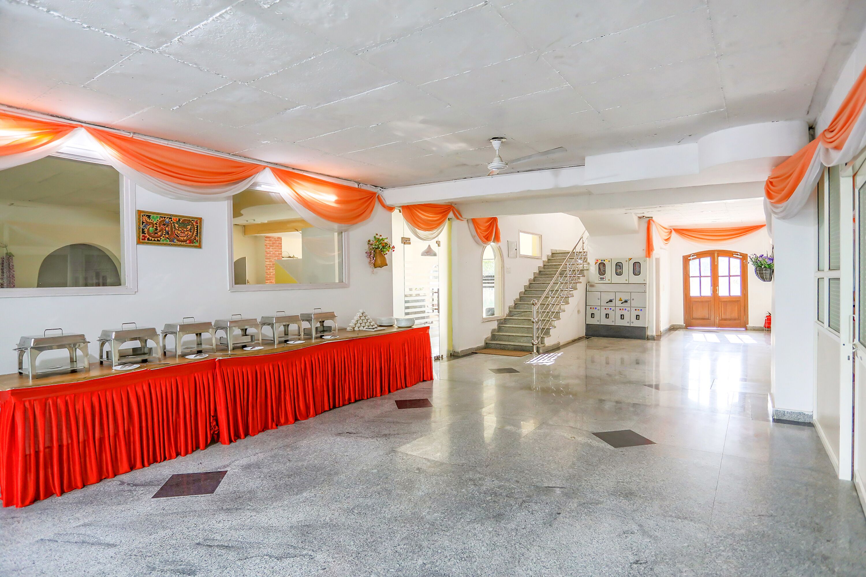 A spacious hall with a long red table, white walls, and orange drapery.